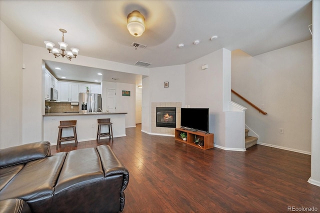 living room featuring stairway, dark wood finished floors, visible vents, a chandelier, and a tile fireplace