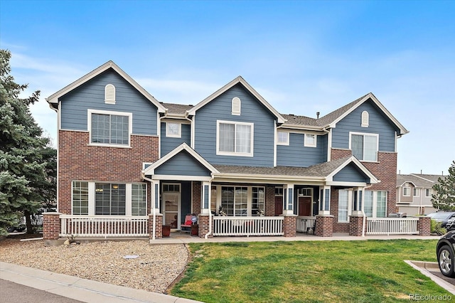 view of front of property with a porch, a shingled roof, brick siding, and a front yard