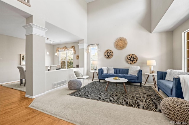 living room featuring visible vents, a towering ceiling, ornate columns, and wood finished floors