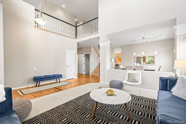 living area with stairway, baseboards, wood finished floors, and a towering ceiling