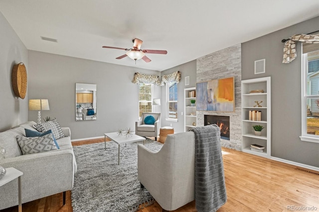 living room featuring built in features, wood finished floors, visible vents, ceiling fan, and a large fireplace