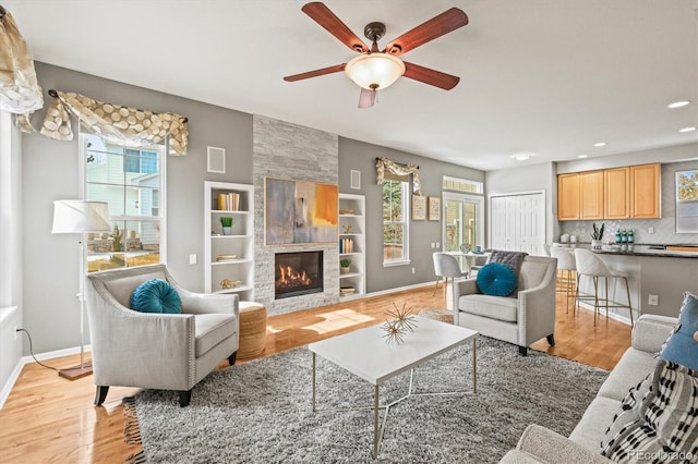 living area featuring baseboards, a large fireplace, light wood-style floors, and ceiling fan