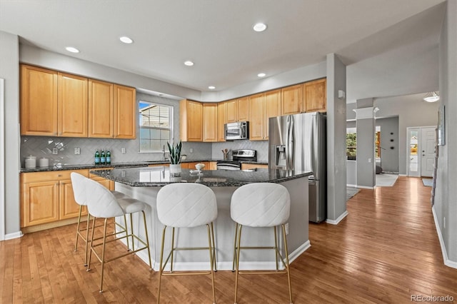 kitchen with light wood-type flooring, a kitchen breakfast bar, a kitchen island, backsplash, and stainless steel appliances