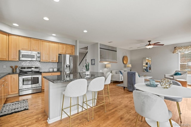 kitchen with light wood-style flooring, a kitchen island, stainless steel appliances, a breakfast bar area, and decorative backsplash