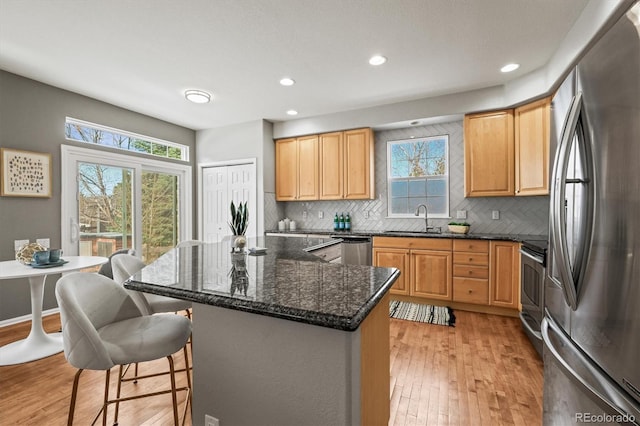 kitchen featuring a kitchen island, light wood-type flooring, a kitchen bar, appliances with stainless steel finishes, and a sink