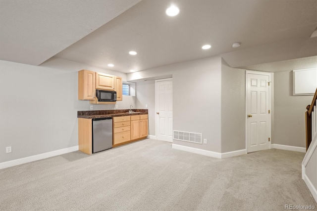 kitchen with visible vents, black microwave, light brown cabinetry, light colored carpet, and a sink