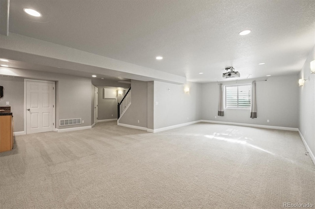 basement with light carpet, visible vents, stairs, and baseboards