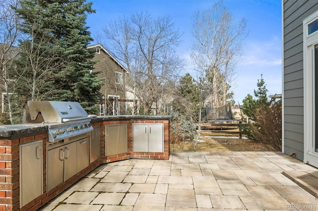 view of patio featuring a grill, exterior kitchen, a trampoline, and fence