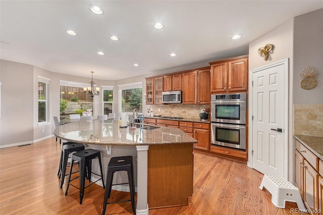 kitchen with a kitchen island with sink, sink, appliances with stainless steel finishes, tasteful backsplash, and a notable chandelier