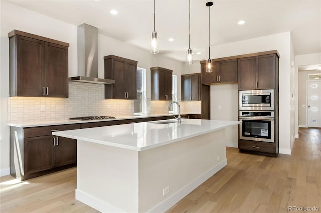 1711 Branching Canopy Dr, Windsor, CO 80550 - kitchen with appliances with stainless steel finishes, wall chimney range hood, light wood finished floors, tasteful backsplash, and recessed lighting