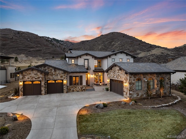 view of front of house featuring driveway, stone siding, a tiled roof, an attached garage, and a mountain view