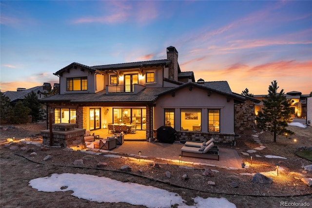 8033 Galileo Way, Littleton, CO 80125 - back of house at dusk featuring a chimney, a balcony, a tile roof, a patio area, and stucco siding