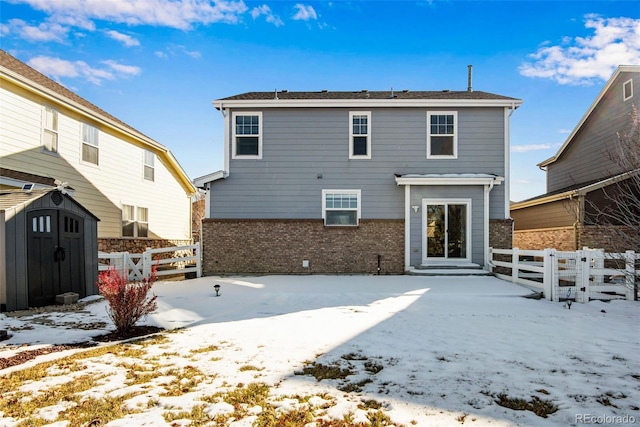 snow covered rear of property featuring a storage unit