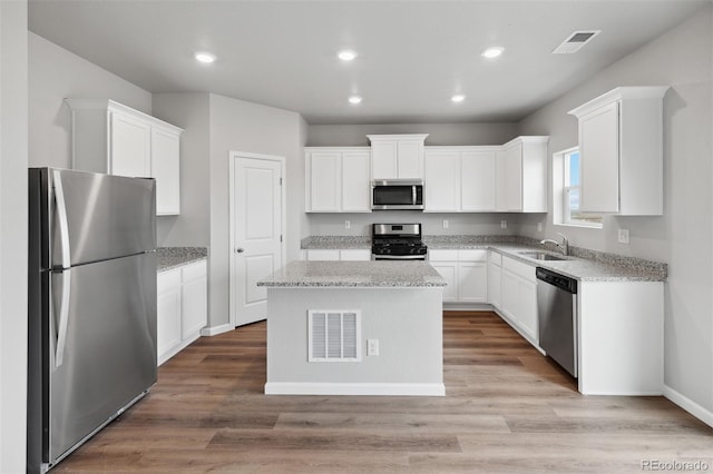 kitchen with appliances with stainless steel finishes, white cabinetry, light hardwood / wood-style flooring, and a kitchen island