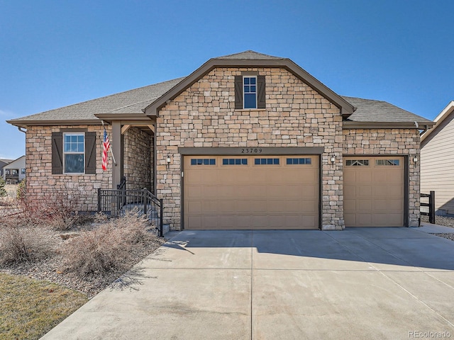 view of front of property featuring stone siding, concrete driveway, a garage, and a shingled roof