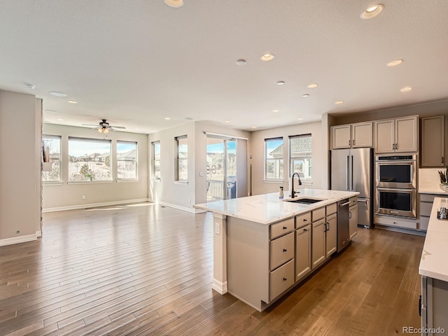 kitchen with a kitchen island with sink, dark wood-style flooring, stainless steel appliances, a sink, and open floor plan