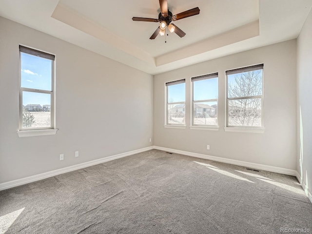 carpeted spare room with a tray ceiling, visible vents, baseboards, and ceiling fan