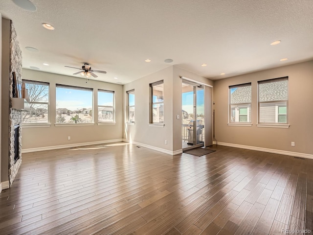 unfurnished living room with a stone fireplace, a textured ceiling, dark wood-type flooring, and baseboards