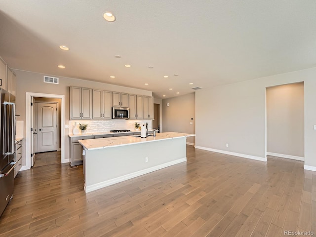 kitchen with stainless steel microwave, gray cabinets, wood finished floors, and visible vents