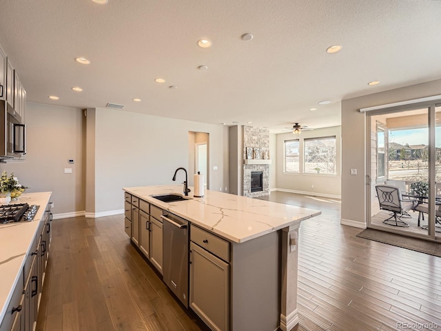 kitchen featuring dark wood-type flooring, a stone fireplace, gray cabinets, appliances with stainless steel finishes, and a sink