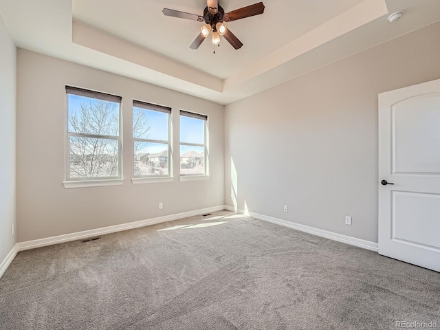 empty room with visible vents, baseboards, carpet flooring, a raised ceiling, and a ceiling fan