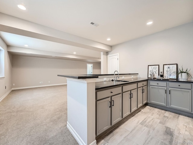 kitchen featuring visible vents, gray cabinets, a sink, dark countertops, and light colored carpet