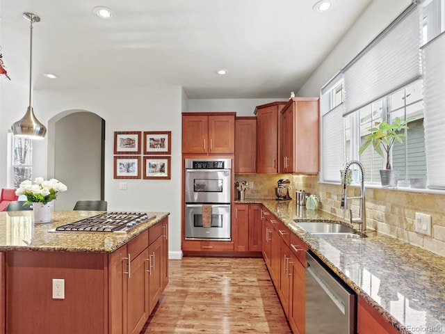 kitchen featuring stainless steel appliances, light stone countertops, sink, and hanging light fixtures