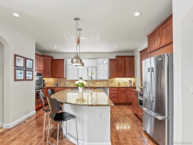 kitchen with light stone countertops, a kitchen breakfast bar, pendant lighting, a kitchen island, and appliances with stainless steel finishes