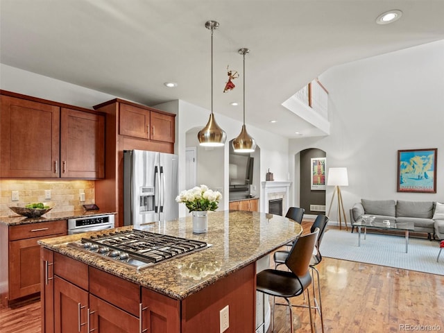 kitchen with dark stone countertops, appliances with stainless steel finishes, decorative light fixtures, a kitchen island, and a breakfast bar area