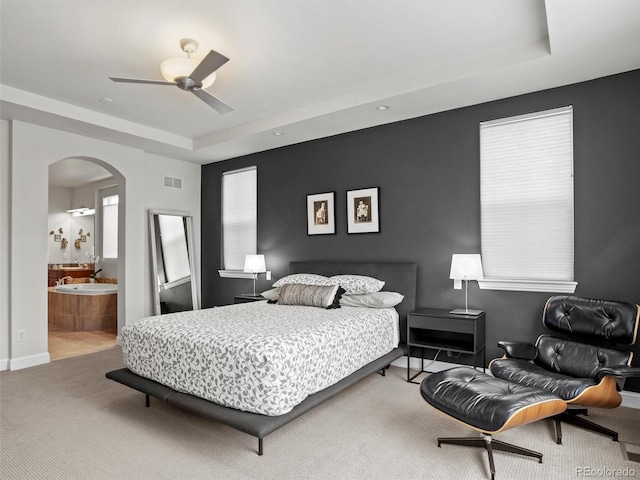 bedroom featuring carpet flooring, ensuite bathroom, a raised ceiling, and ceiling fan