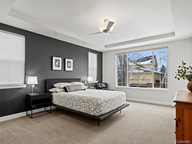 bedroom with light colored carpet, a raised ceiling, and ceiling fan