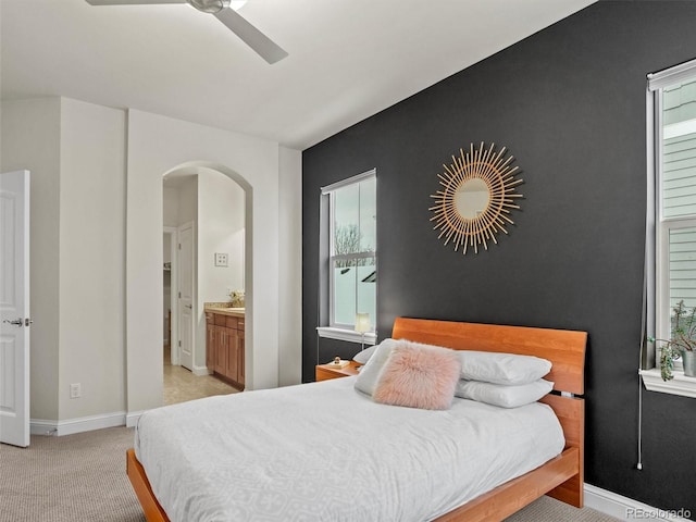 bedroom featuring ensuite bath, ceiling fan, light colored carpet, and multiple windows