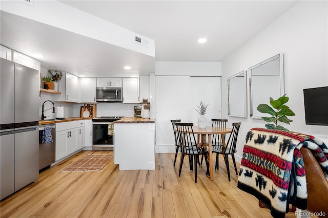 kitchen featuring stainless steel appliances, butcher block counters, white cabinetry, and a sink