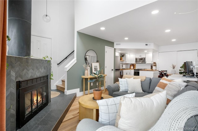 living area with a tiled fireplace, recessed lighting, stairway, and wood finished floors