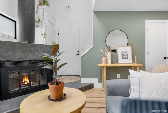 living area with a glass covered fireplace, baseboards, and wood finished floors