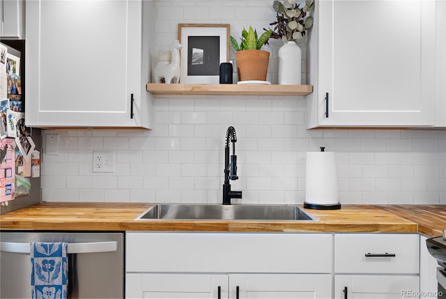 kitchen with stainless steel dishwasher, wood counters, white cabinets, and a sink