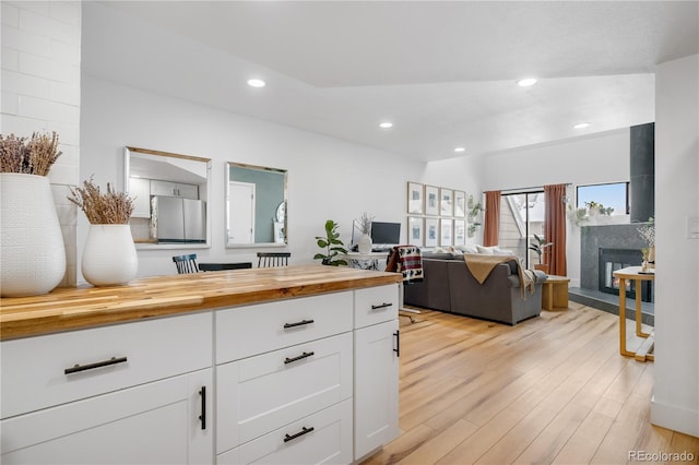 kitchen with butcher block counters, light wood-type flooring, white cabinetry, recessed lighting, and a premium fireplace