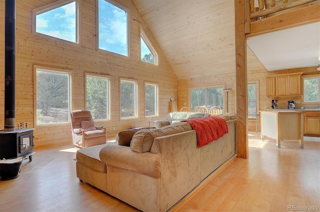 living room featuring light wood-style flooring, wood walls, high vaulted ceiling, and a wood stove