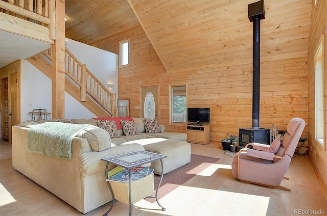 living area featuring high vaulted ceiling, a wood stove, stairs, wood ceiling, and a wealth of natural light