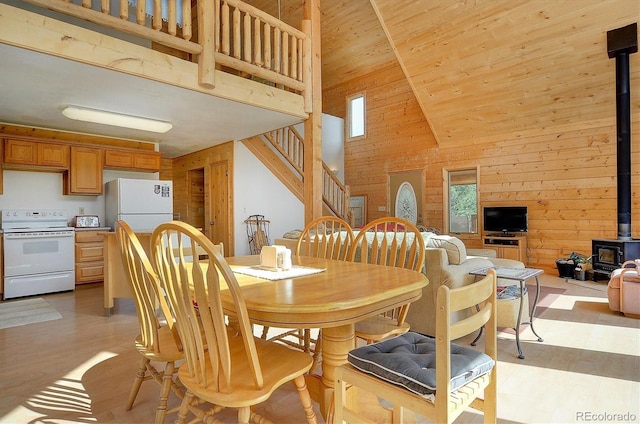 dining area featuring stairs, light wood-style floors, wood walls, and a wood stove