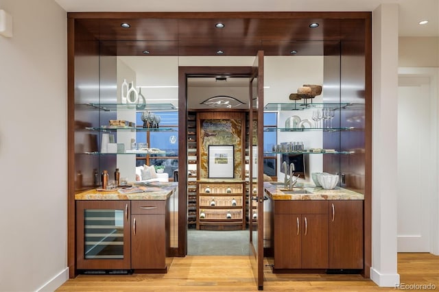 bar featuring sink, beverage cooler, light stone countertops, and light hardwood / wood-style floors