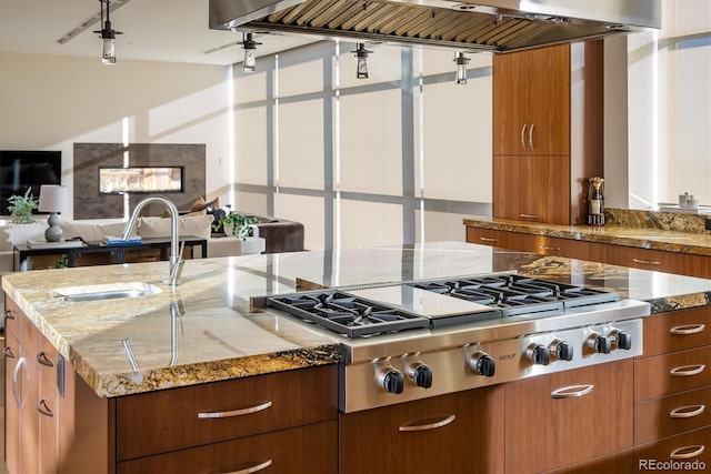 kitchen with a kitchen island with sink, sink, wall chimney exhaust hood, and stainless steel gas stovetop