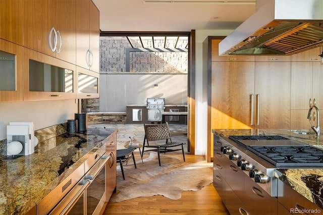 kitchen featuring stainless steel gas cooktop, island range hood, light wood-type flooring, and dark stone counters