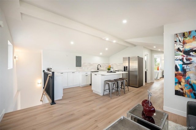 kitchen with a kitchen breakfast bar, light hardwood / wood-style flooring, stainless steel fridge, a center island, and lofted ceiling with beams