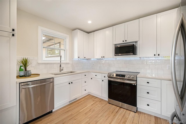 kitchen featuring backsplash, white cabinetry, light hardwood / wood-style flooring, sink, and stainless steel appliances