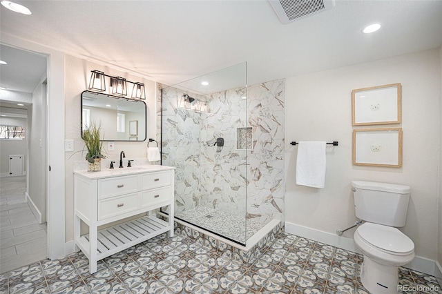 bathroom with toilet, vanity, a tile shower, and tile patterned floors