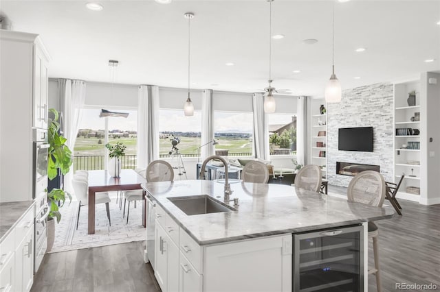 19887 Kershaw Ct, Monument, CO 80132 - kitchen featuring beverage cooler, dark wood finished floors, a stone fireplace, a center island with sink, and a ceiling fan