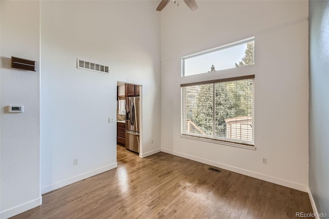 unfurnished room with ceiling fan, a high ceiling, and light hardwood / wood-style flooring