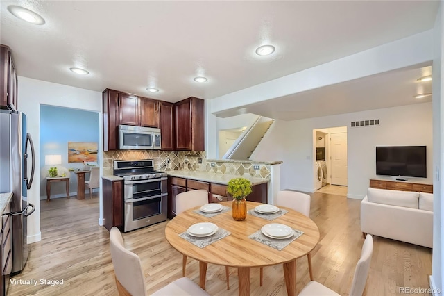 kitchen featuring independent washer and dryer, stainless steel appliances, light hardwood / wood-style flooring, and tasteful backsplash