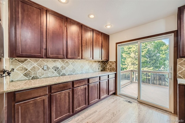 kitchen featuring light stone countertops, decorative backsplash, and light wood-type flooring